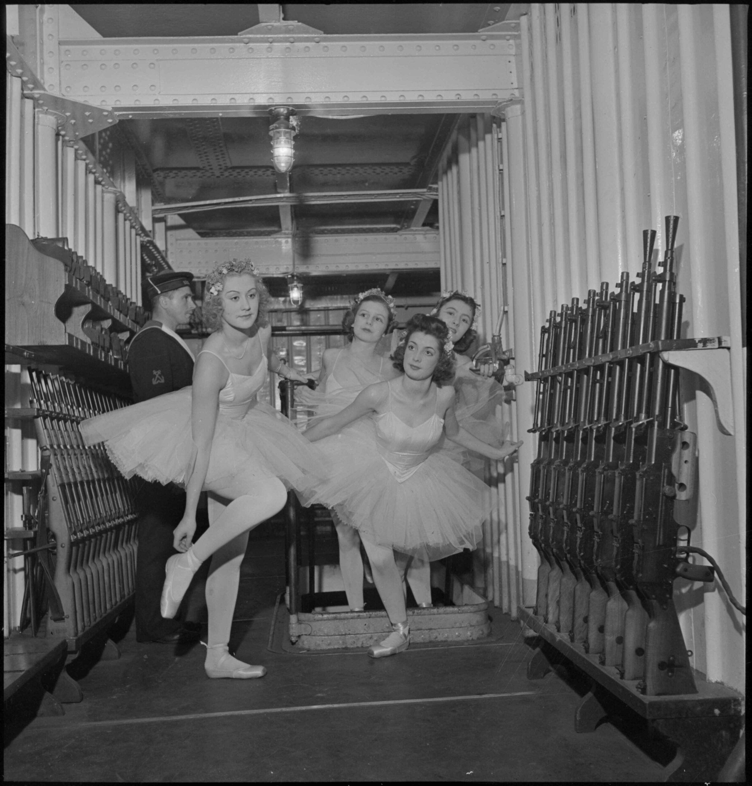 Des danseuses d'un corps de ballet traversent l'armurerie du porte-avions Béarn à bord duquel elles se produisent la veille de Noël. 
24 décembre 1939, Brest